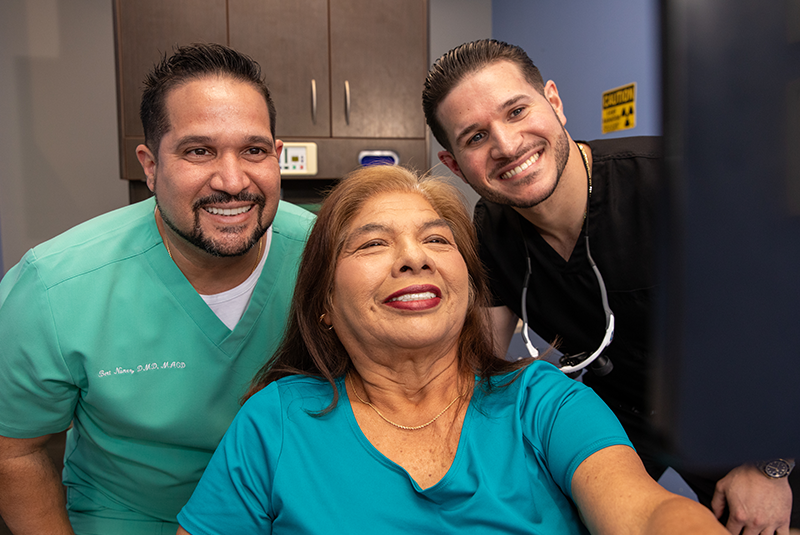 Dr. Nunez and Dr Perez with a patient holding a mirror and smiling